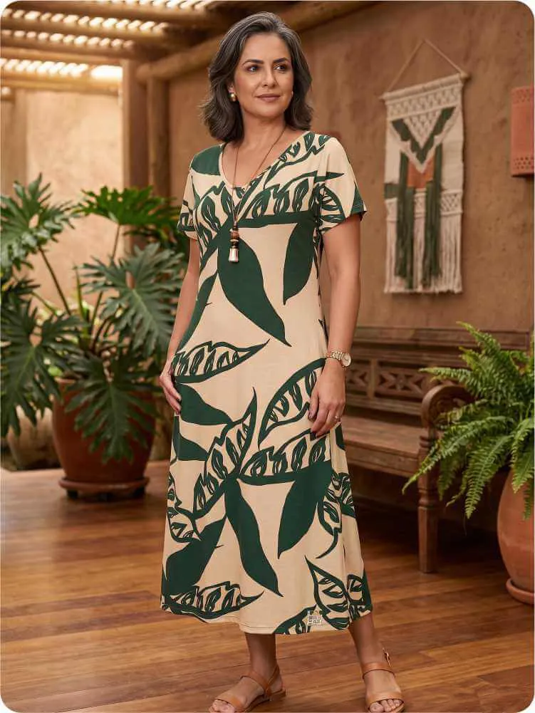 Modelo vestindo vestido para evento social midi em malha bege com estampa folhada verde musgo, decote V e mangas curtas.